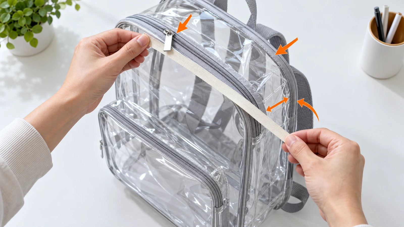 Hände messen mit einem einfachen Maßband die äußere Höhe, Breite und Seitenfaltentiefe eines durchsichtigen PVC-Rucksacks; Pfeile zeigen, dass Reißverschlussschieber und Einfassung zur Größe zählen