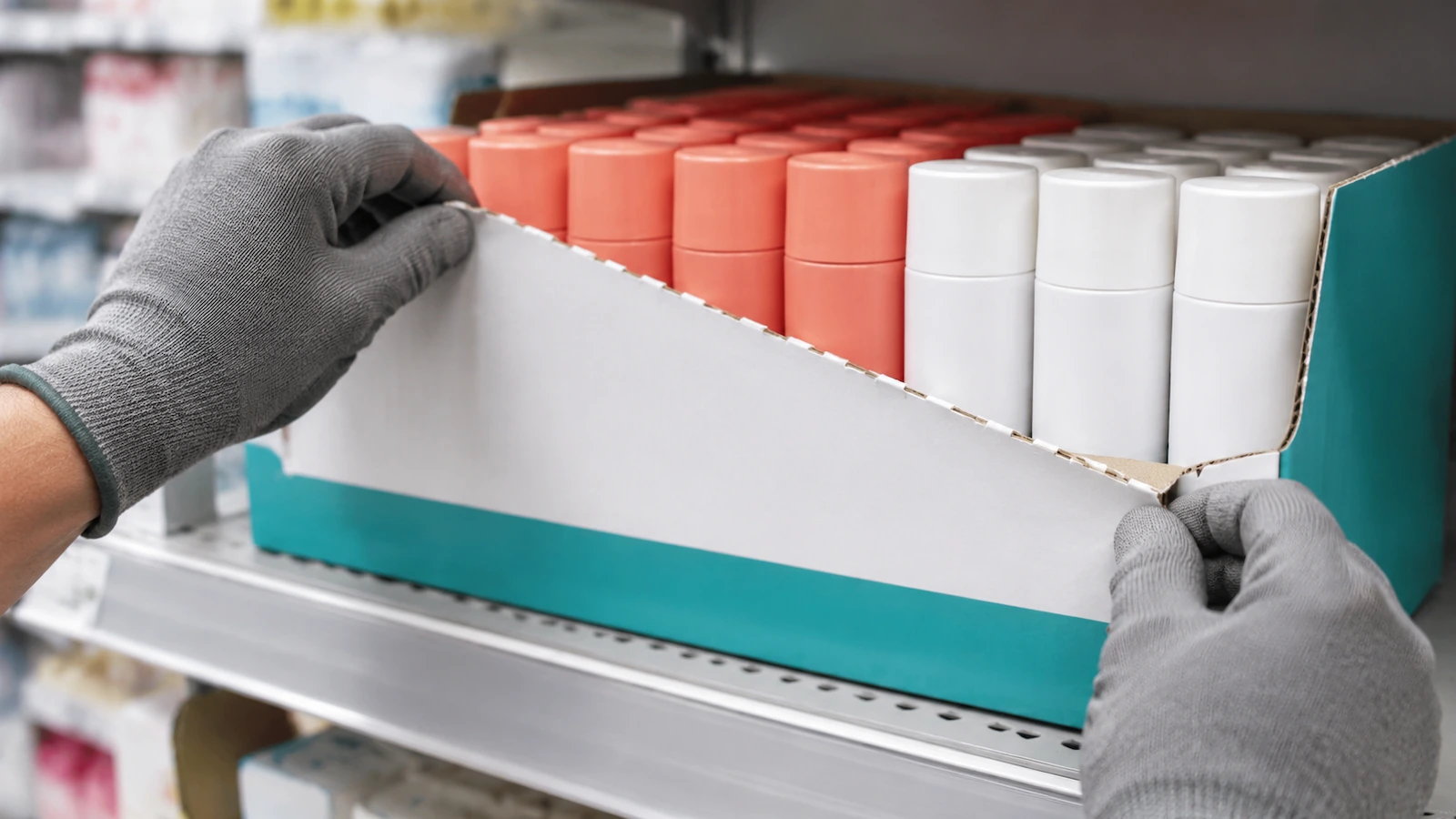 Hände ziehen die perforierte Frontabdeckung eines regalfertigen Trays aus Wellpappe ab und legen ordentlich angeordnete, regalfertige Ware frei
