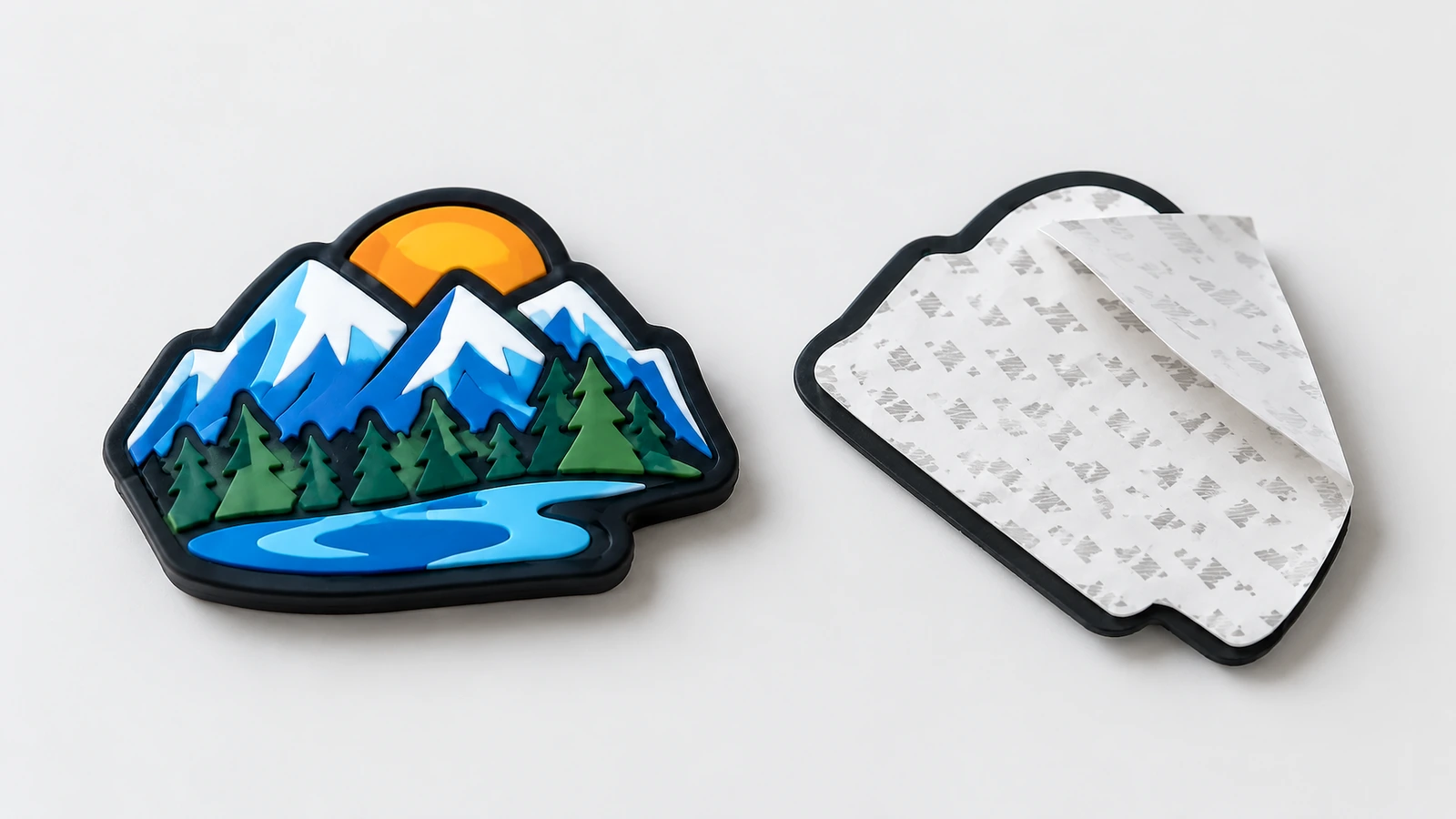 Weiches PVC-Etikett mit Bergmotiv, mit der Vorderseite nach oben neben seiner Klebrückseite und einem teilweise abgezogenen Trägerpapier